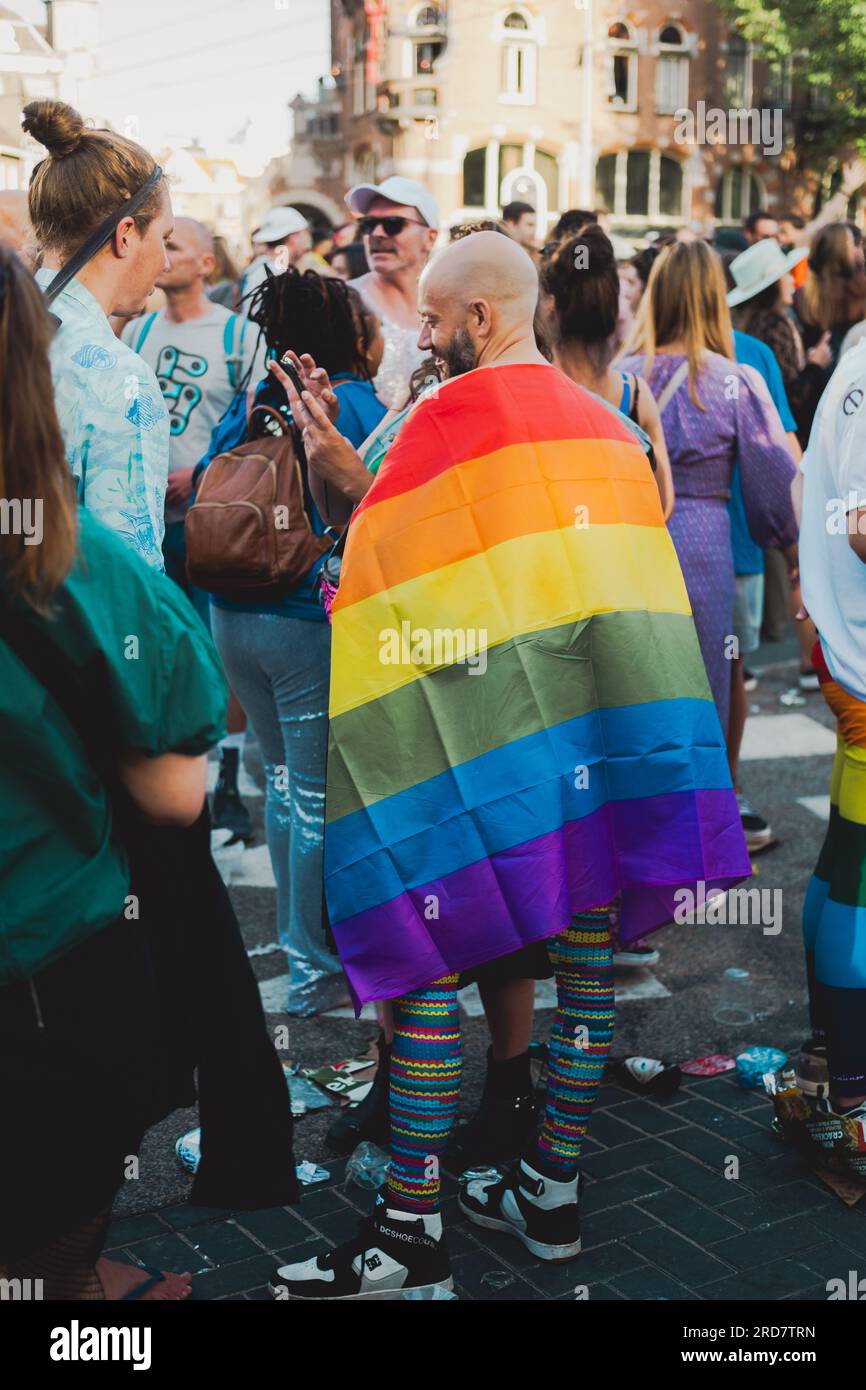 Amsterdam, Niederlande – 6. August 2022: Ein glatzköpfiger, lächelnder Mann mit einer Regenbogenflagge steht mitten in der Menge und feiert Pride Amsterdam Stockfoto