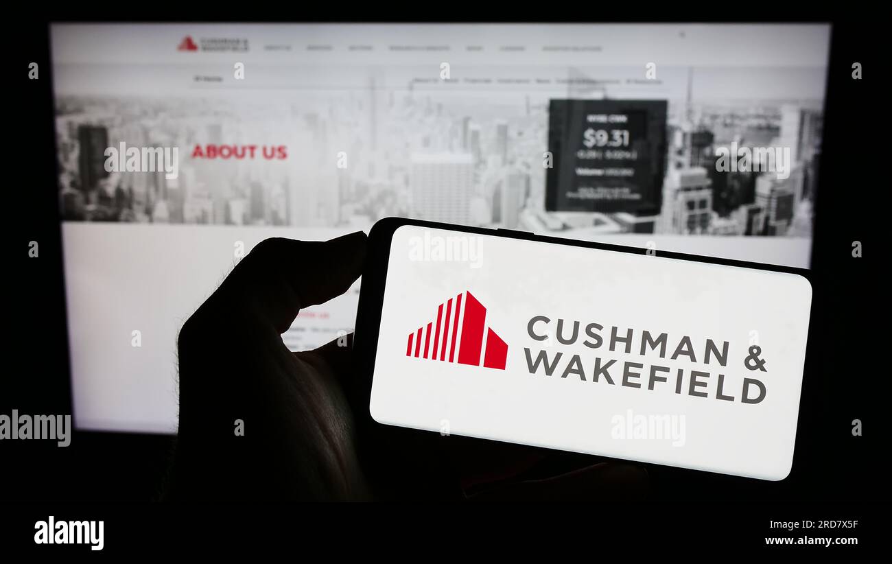 Person, die ein Mobiltelefon mit dem Logo der Immobilienfirma Cushman Wakefield plc auf dem Bildschirm vor der Webseite hält. Konzentrieren Sie sich auf das Display des Telefons. Stockfoto