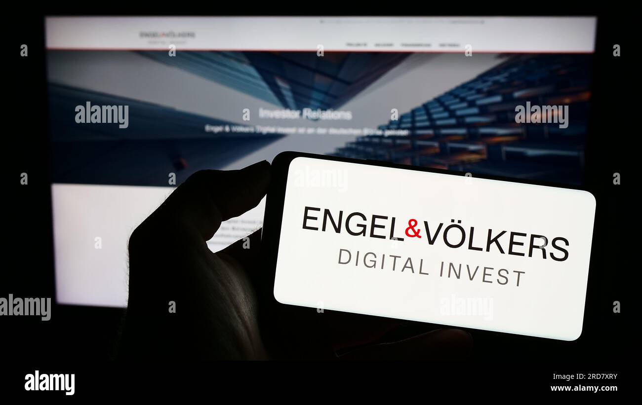 Person, die ein Mobiltelefon mit dem Logo der deutschen Immobiliengesellschaft EV Digital Invest AG auf dem Bildschirm vor der Webseite hält. Konzentrieren Sie sich auf das Display des Telefons. Stockfoto