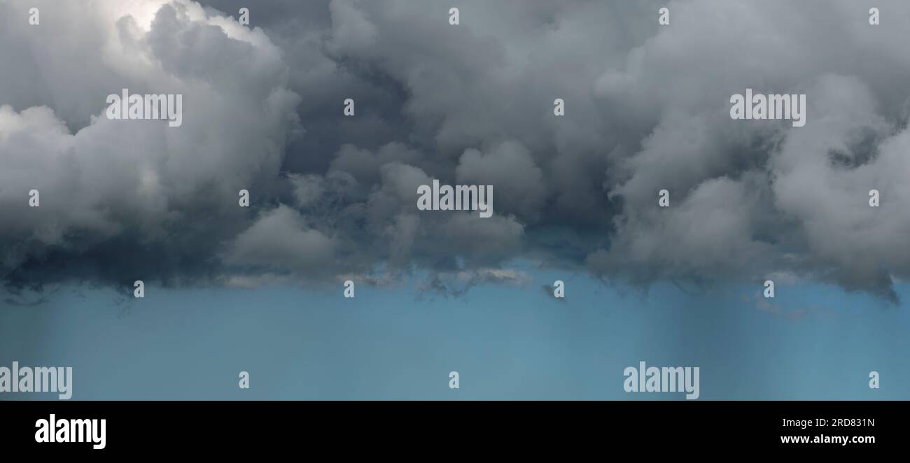 Bedrohliche Wolkenschichten, die eine gerade Linie bilden, mit einem Streifen klaren Himmels, der einen dunkleren Abstrich von Regen zeigt, Panorama. Stockfoto