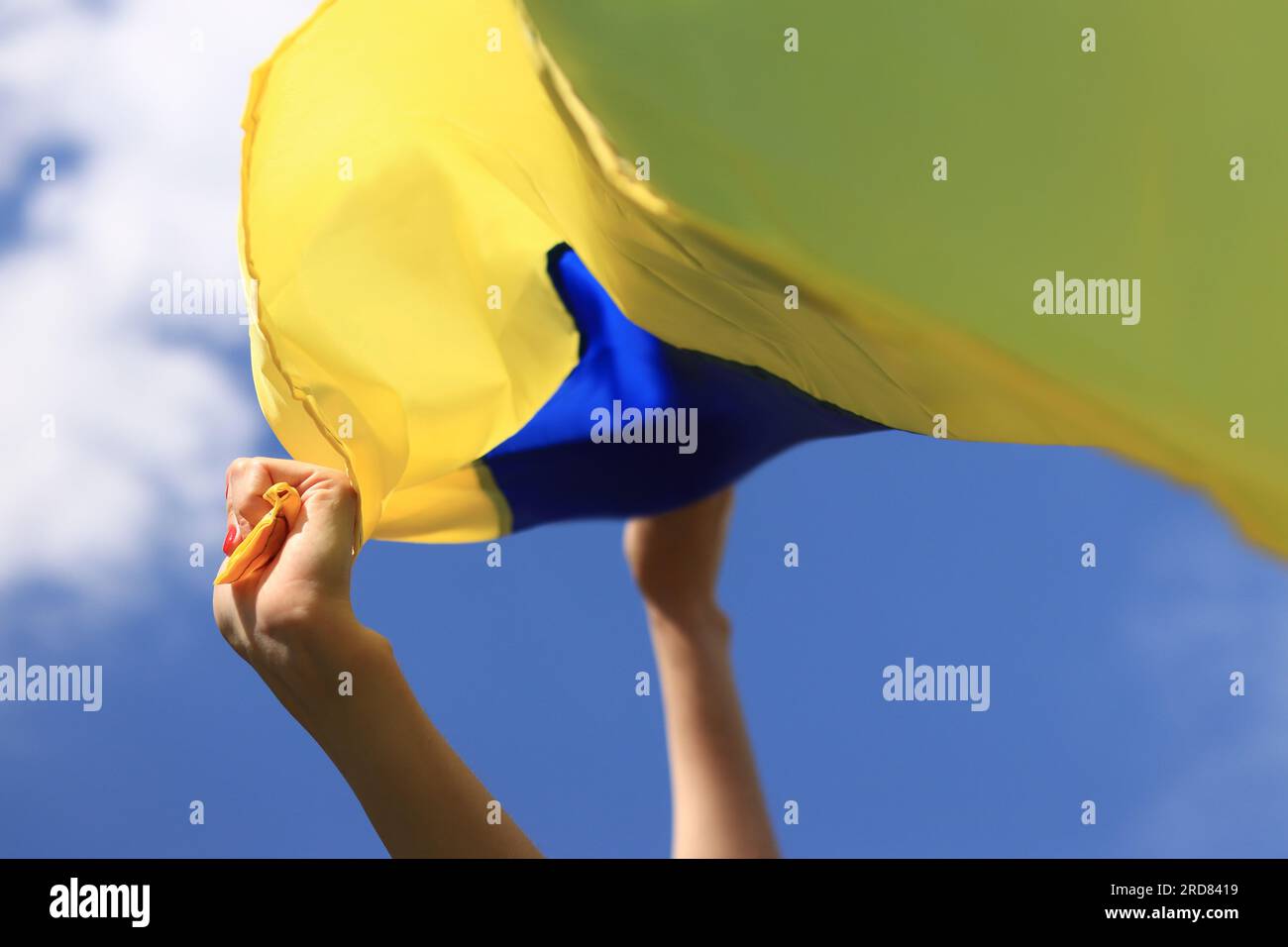 Frauenhände mit der ukrainischen Flagge am Himmel. Die ukrainische Flagge flattert im Wind. Unabhängigkeitstag der Ukraine. Gelb-blaue Flagge Stockfoto