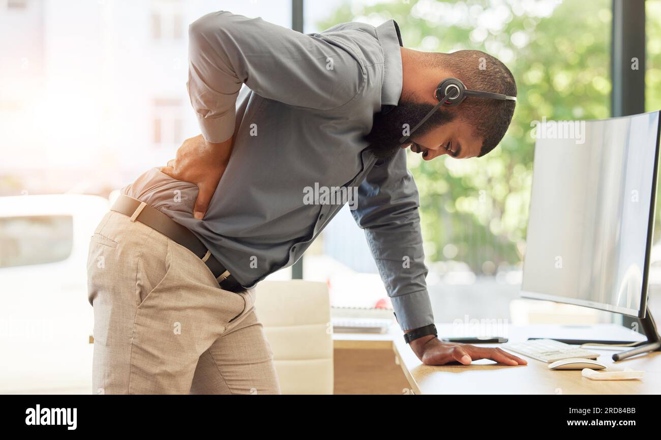 Callcenter, Rückenschmerzen und ein schwarzer Berater in seinem Büro, stehen und halten ist Wirbelsäule. Verletzung, Kundendienst oder Unterstützung und ein junger Mann Stockfoto