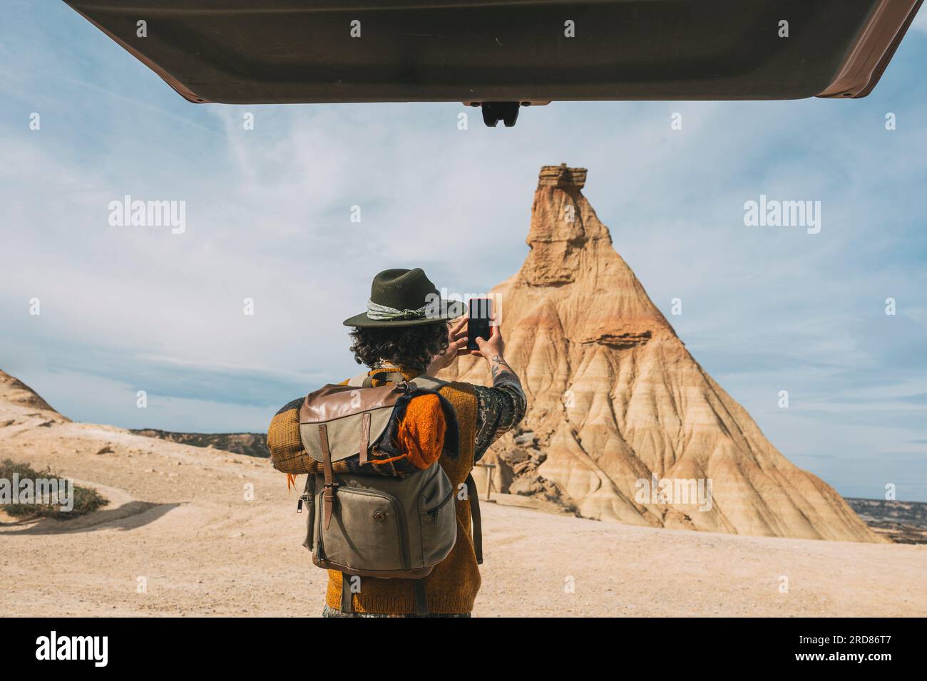 Rückansicht Eines Mannes mit Hut, der Ein Foto mit einem Smartphone von seinem Van in der Bardenas-Wüste macht. Navarra Stockfoto