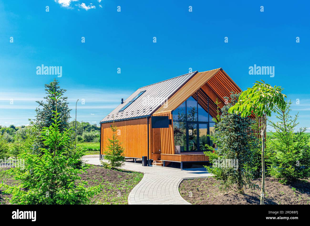 Ein kleines Bauernhaus auf einem Grundstück mit einem Pfad, Bäumen und Büschen unter blauem Himmel Stockfoto