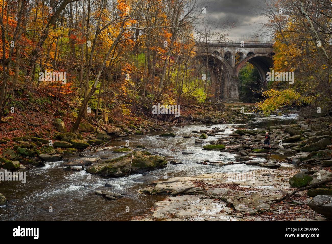 Ein kleiner Junge mit Angelrute steht am Rand des Rocky River im David Fortier Park in Olmsted Falls an einem stürmischen späten Herbsttag. Stockfoto