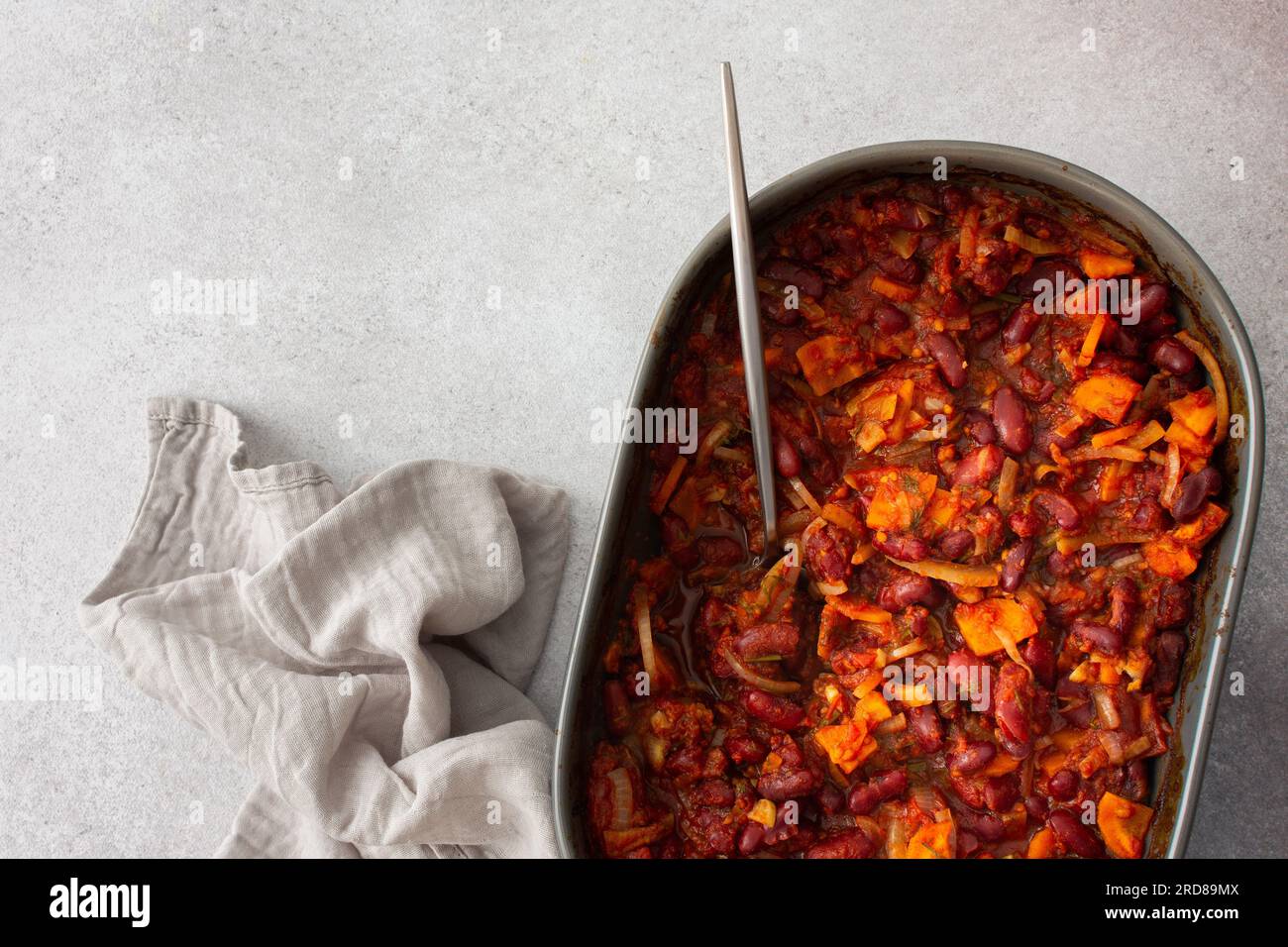 Gesundes Frühstück und Mittagessen, gedünstete rote Bohnen mit Karotten, Zwiebeln und Tomaten, Blick von oben auf eine ovale Keramikrösterei mit gedünsteten Hülsenfrüchten Stockfoto