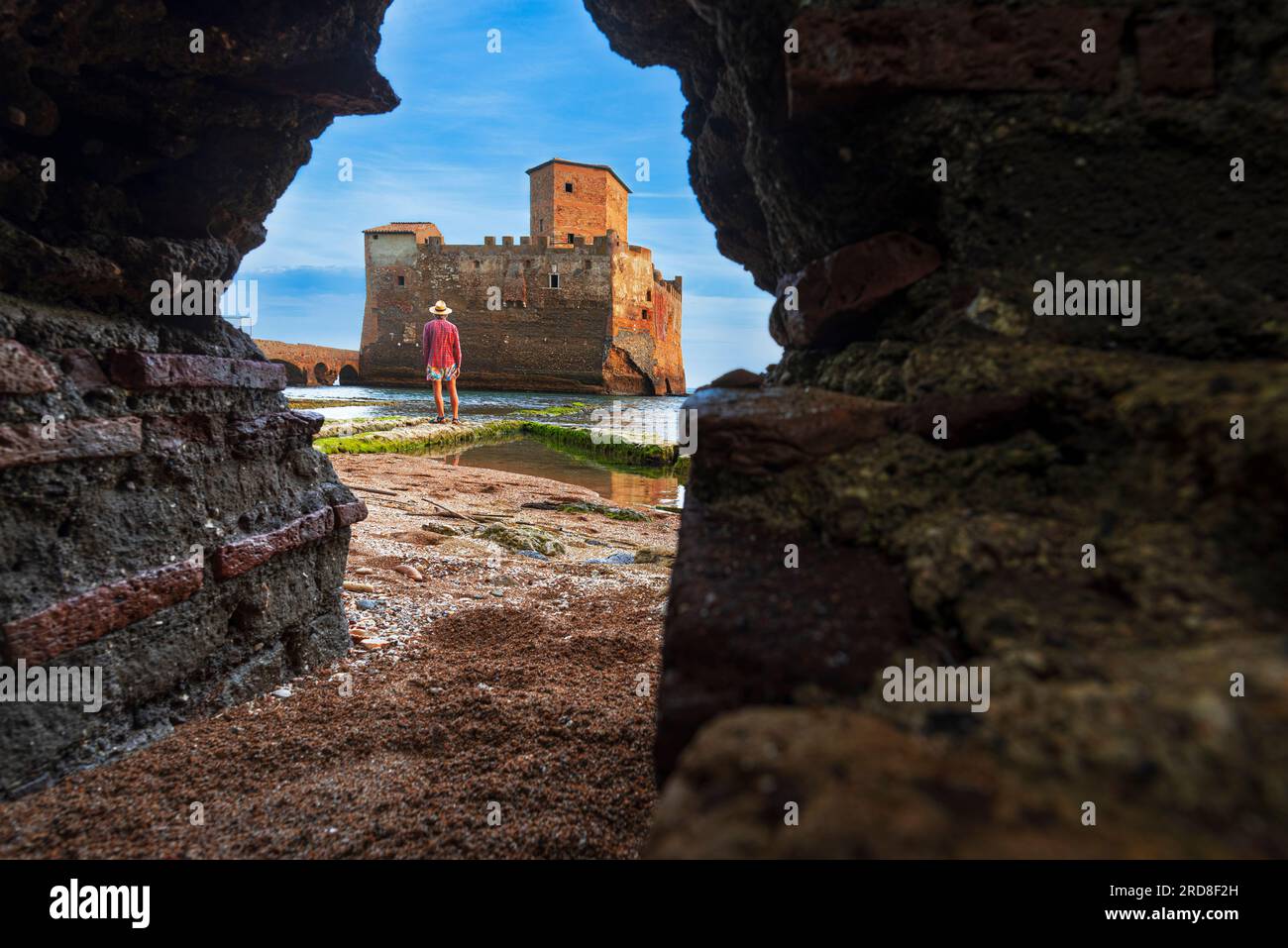 Blick von unten auf einen Mann, der vor dem Schloss Torre Astura steht und durch ein Loch in der Mauer gesehen wird, die Provinz Rom Stockfoto