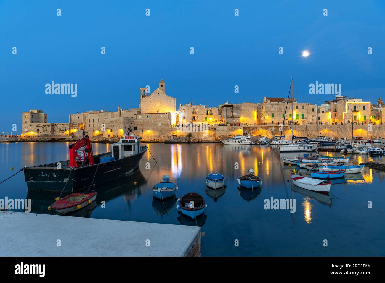 Vollmondnacht über dem beleuchteten mittelalterlichen Dorf Giovinazzo mit touristischem Yachthafen im Vordergrund, Provinz Bari Stockfoto