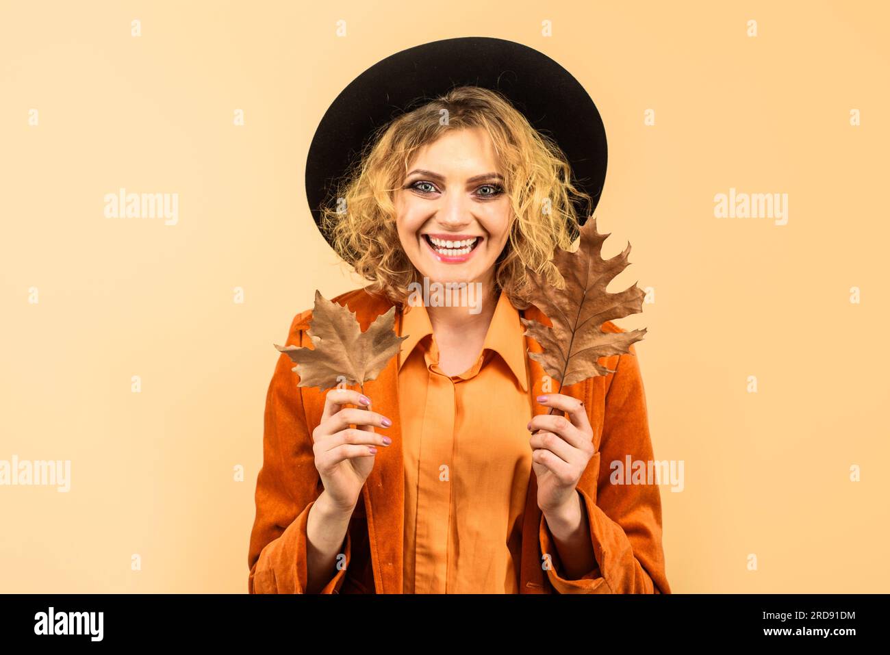 Modetrends für den Herbst. Lächelnde Herbstfrau mit schwarzem Hut und Herbstlaub. Hübsches Mädchen in orangefarbenem Hemd und Mantel mit Herbstblättern. Herbst Stockfoto