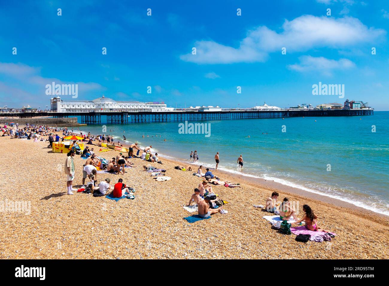 Leute, die an einem heißen Sommertag am Strand sitzen, mit Brighton Palace Pier im Hintergrund, Brighton, Großbritannien Stockfoto