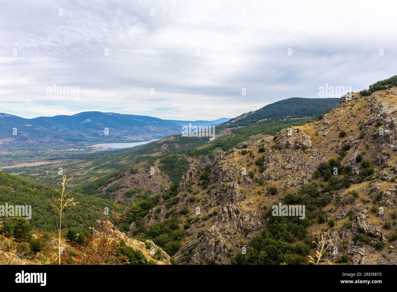 Felsige Berge im zentralen System in Spanien, Landschaft mit Pinilla del Valle Dorf und Pinilla Reservoir in der Ferne, Blick von der M-611 Straße. Stockfoto