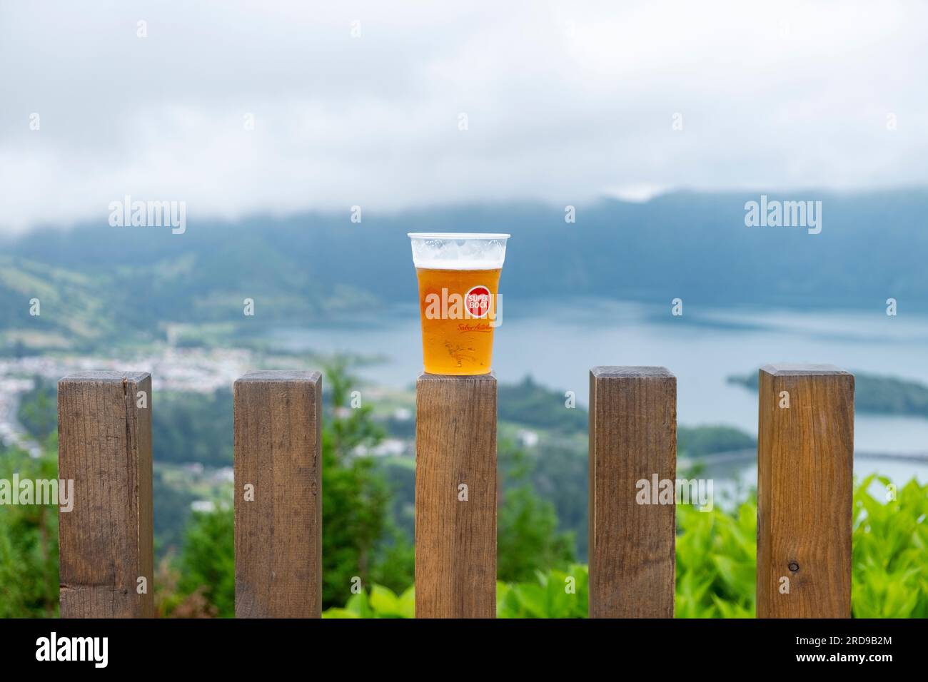 São Miguel, Azoren - 27.07.2019 Uhr: Ein Glas "Super Book - Sabor Autêntico" auf einem Holzzaun mit Blick auf den See "Lagoa das Sete CI" in den sieben Städten Stockfoto