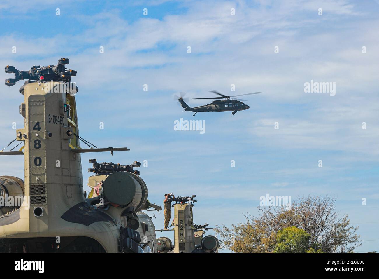 Ein UH-60m Black Hawk, der Task Force Warhawk, 16. Combat Aviation Brigade, zugewiesen wurde, führt einen Wartungstestflug durch, während ein Betreuer sich darauf vorbereitet, die Flügel eines CH-47 Chinook Hubschraubers während des Hafenbetriebs wieder anzubringen, um die Übung Talisman Sabre 23 im Hafen von Gladstone, Queensland, Australien, vorzubereiten, Juli 17. 2023. Talisman Sabre ist die größte bilaterale Militäraktion zwischen Australien und den Vereinigten Staaten, die ein freies und offenes Indo-Pacific vorantreibt, indem sie die Beziehungen und die Interoperabilität zwischen wichtigen Verbündeten stärkt und unsere kollektiven Fähigkeiten verbessert, um auf eine breite Arr zu reagieren Stockfoto