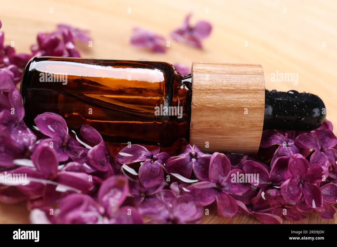 Flasche mit ätherischem Öl und Fliederblumen auf Holzoberfläche, Nahaufnahme Stockfoto