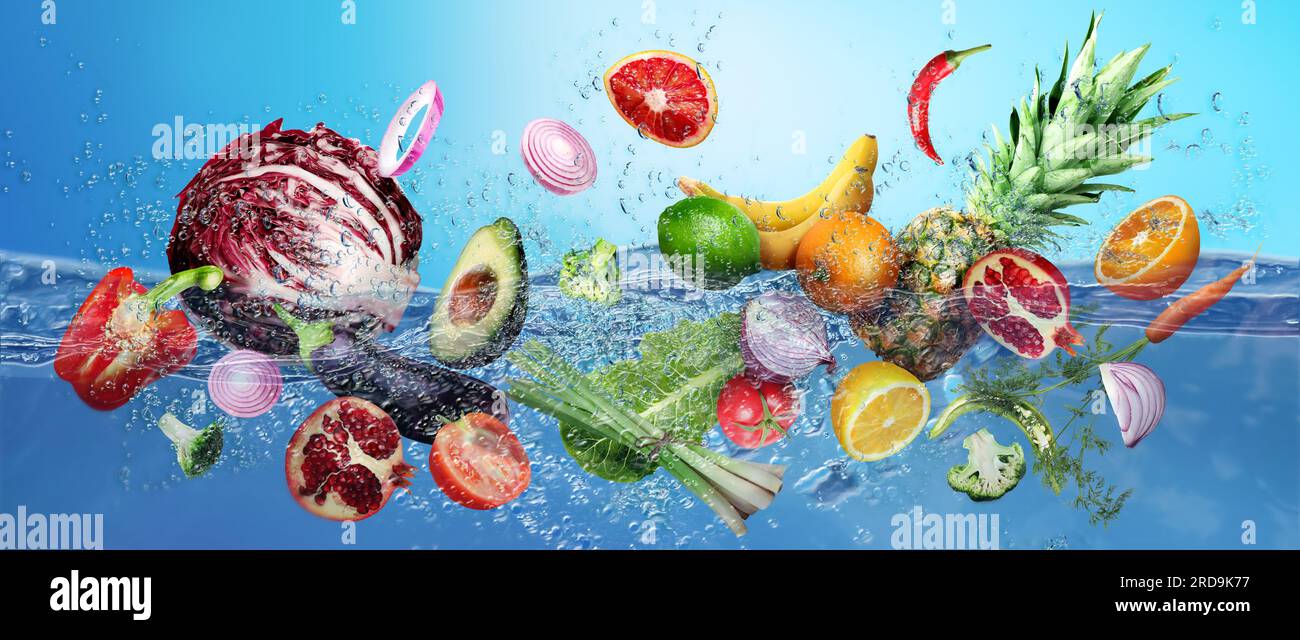 Viele Früchte und Gemüse fallen vor blauem Hintergrund ins Wasser Stockfoto