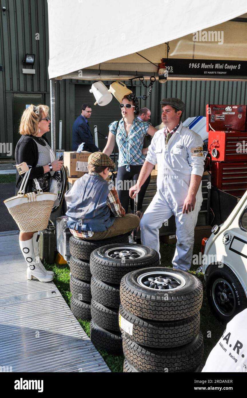 Leute in Oldtimer-Kleidung in einer Garage für einen Rennwagen Mini bei der Goodwood Revival Oldtimer-Motorsportveranstaltung in West Sussex, Großbritannien. Paddock-Szene Stockfoto