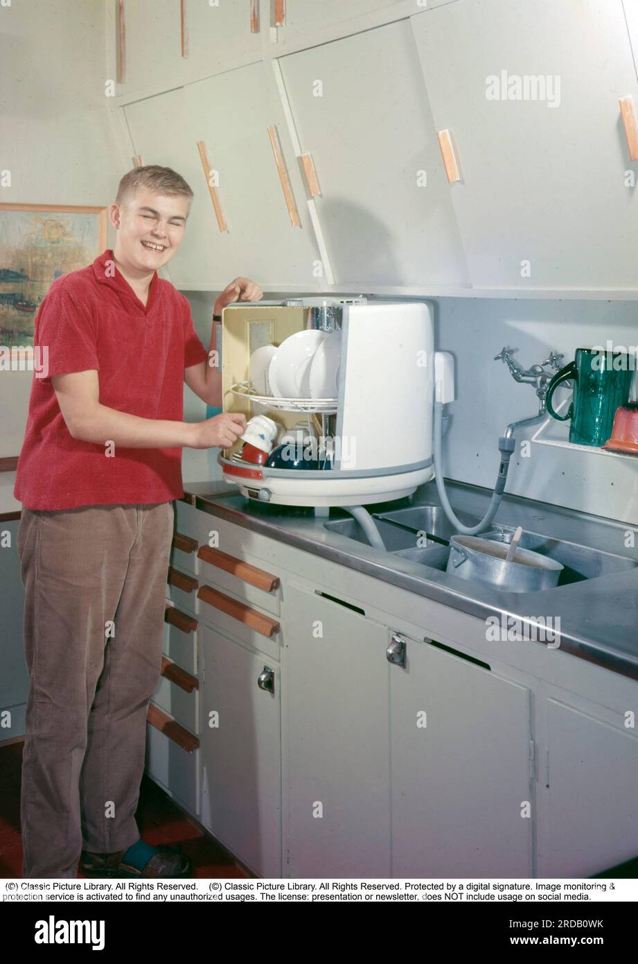 Küche in der Vergangenheit. Ein junger Mann von der schwedischen Firma Electrolux's erster Geschirrspüler, der Tisch-Geschirrspüler D10, nannte den runden Becher oder die runde Dose, der 1959 mit der Produktion begann und dann 410 SEK zzgl. MwSt. kostete. Der Geschirrspüler war bis 1973 in Produktion und wurde in 50.000 Exemplaren produziert. Der große Unterschied zu modernen Geschirrspülern war, dass sich die Schnur Körbe mit den schmutzigen Tellern und Gläsern innen drehten und mit stationären Wasserstrahlen gereinigt wurden. Schweden 1959. Conard Stockfoto