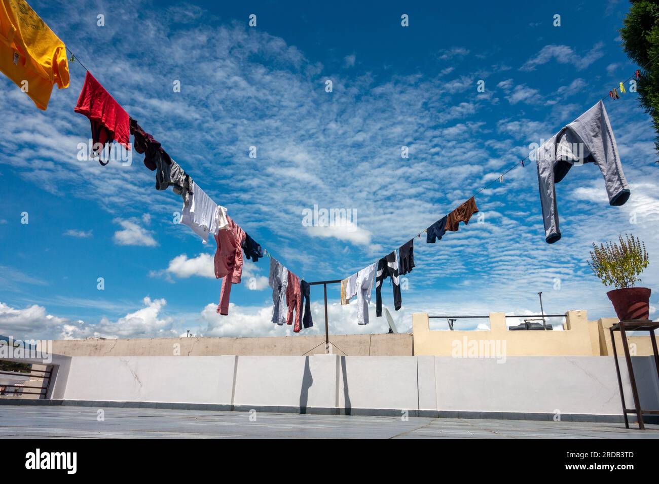 Gewaschene Kleidung, die an einem sonnigen Tag an Linien hing, mit wunderschönem blauen Himmel und weißen Wolken im Hintergrund. Indien. Stockfoto