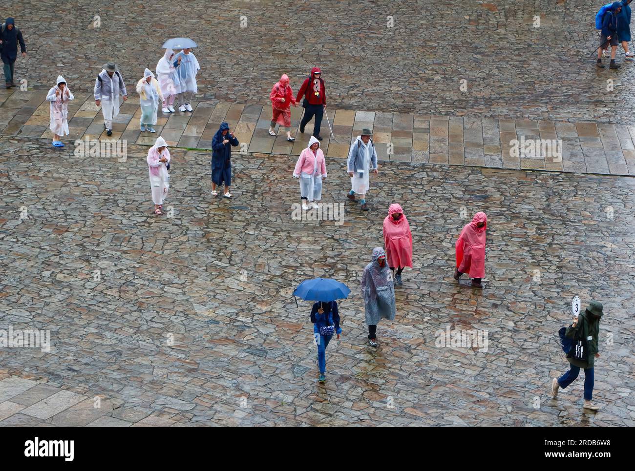 Die mit Stein gepflasterte Plaza de Obradoiro, von oben gesehen an einem regnerischen Juni-Tag mit Touristen, die mit Plastiktüchern unterwegs sind Santiago de Compostela Galicia Spanien Stockfoto