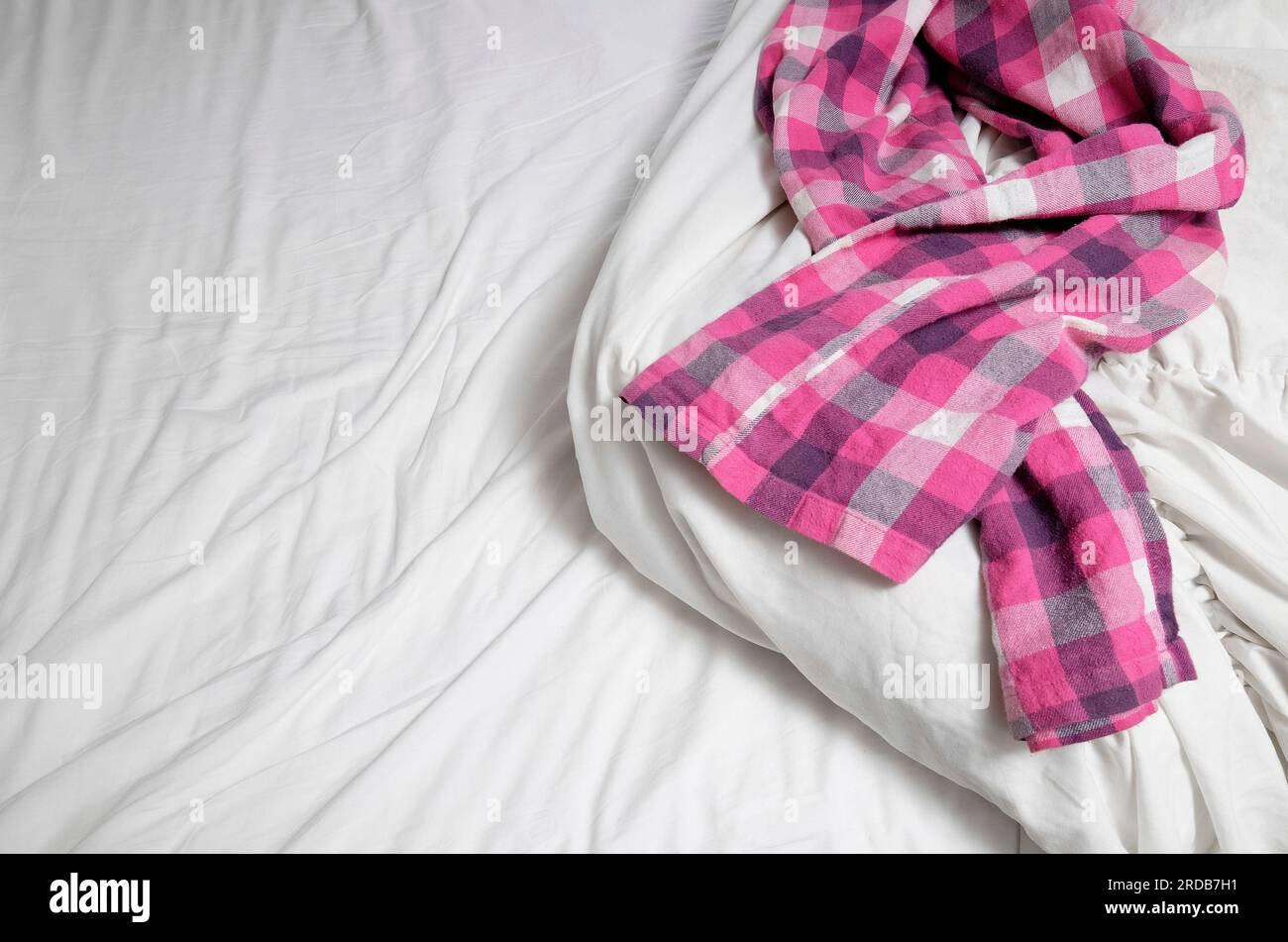 Pinkfarbene Schottenpyjamahose auf ungemachtem Bett Stockfoto