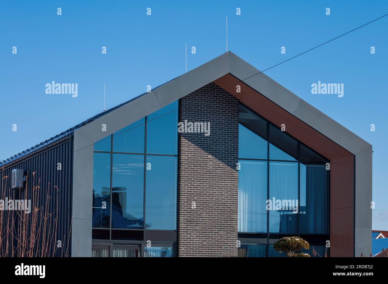 Ein modernes Haus im architektonischen Stil eines Scheunenhauses. Die Fassade ist grau, mit Stahl und Ziegeln und großen Fenstern dekoriert Stockfoto