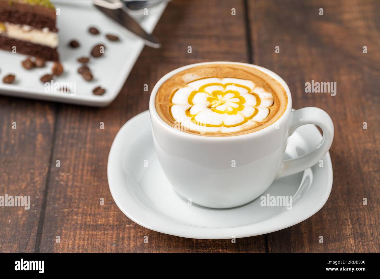 Gemusterter Cappuccino-Kaffee in einer weißen Porzellantasse auf einem Holztisch Stockfoto