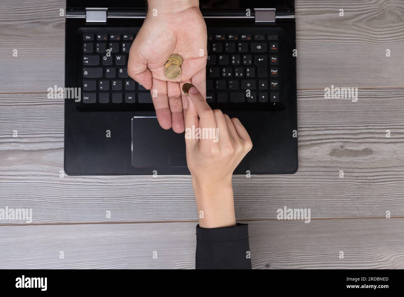 Von oben gesehen, wie eine Hand zahlt und eine andere über einen Computerbildschirm Geld empfängt. Symbolisiert Online-Transaktionen, E-Commerce und das seismische Shif Stockfoto