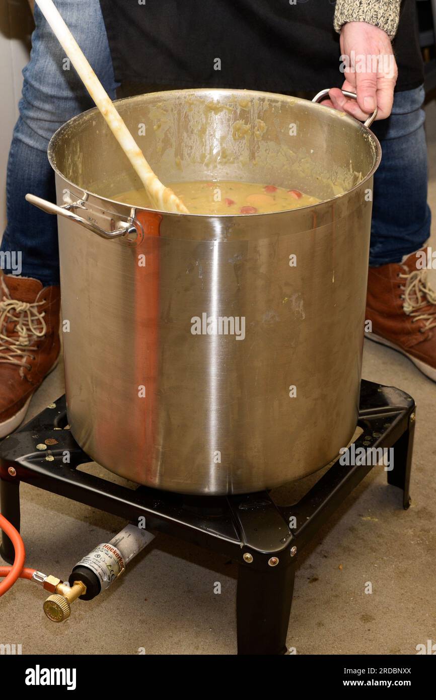 Rühren in einem großen Topf gefüllt mit holländischer Erbsensuppe. Die Pfanne steht auf einem Gasbrenner Stockfoto