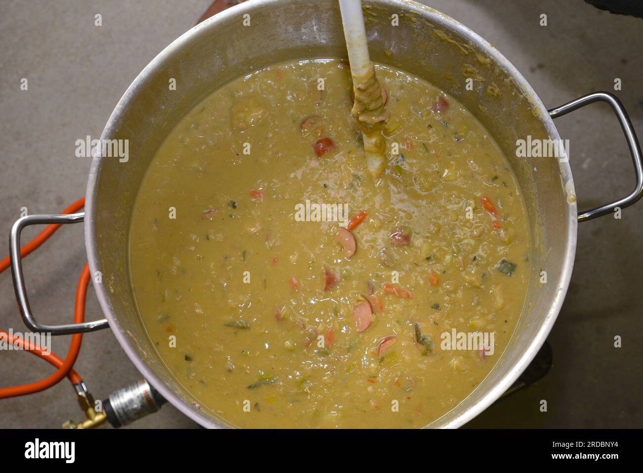 Große Pfanne mit gut gefüllter Erbsensuppe, in der gerührt wird Stockfoto