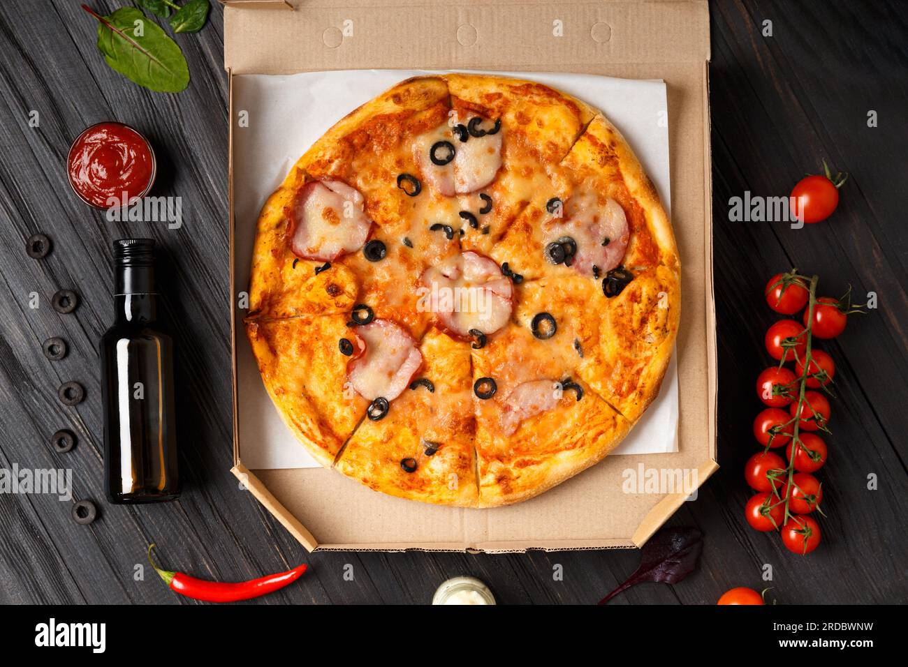 Pizza in offener Schachtel, Saucen, frisches Gemüse auf dunklem Holzhintergrund. Pizzalieferung Stockfoto