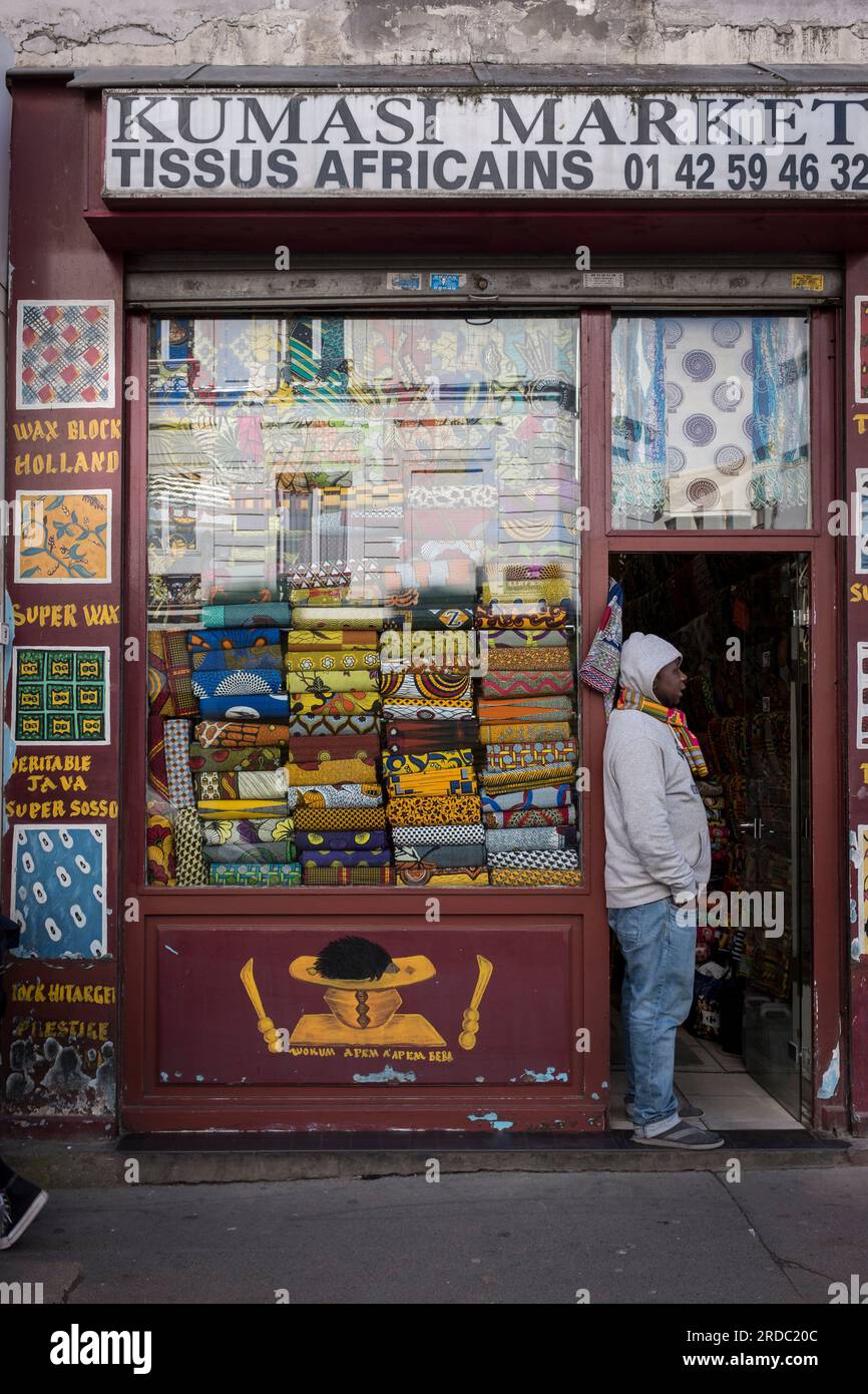 Ein Mann steht vor der Tür eines Ladens, der afrikanische Textilien verkauft, in der vorwiegend nordafrikanischen Nachbarschaft Goutte d'Or im 18. Arrondissement von Paris, Frankreich Stockfoto