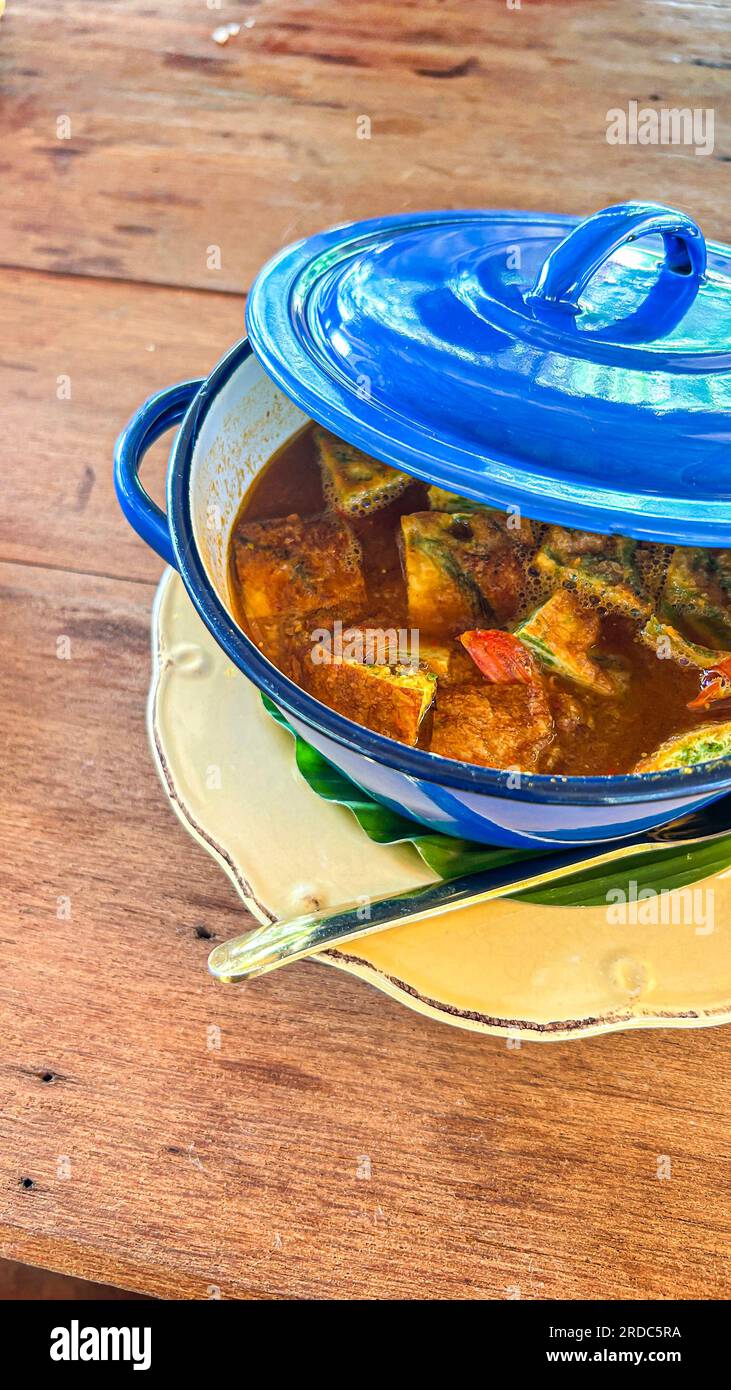 Thailändisches Curry mit gebranntem Ei in blauem Topf auf Holztisch Stockfoto