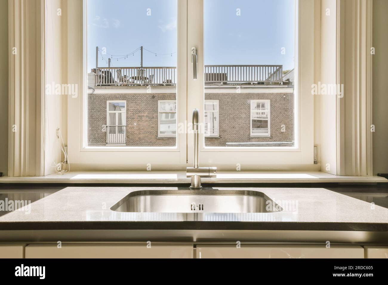 Ein Waschbecken vor einem offenen Fenster mit Blick auf eine Backsteinwand und weiße Vorhänge Stockfoto