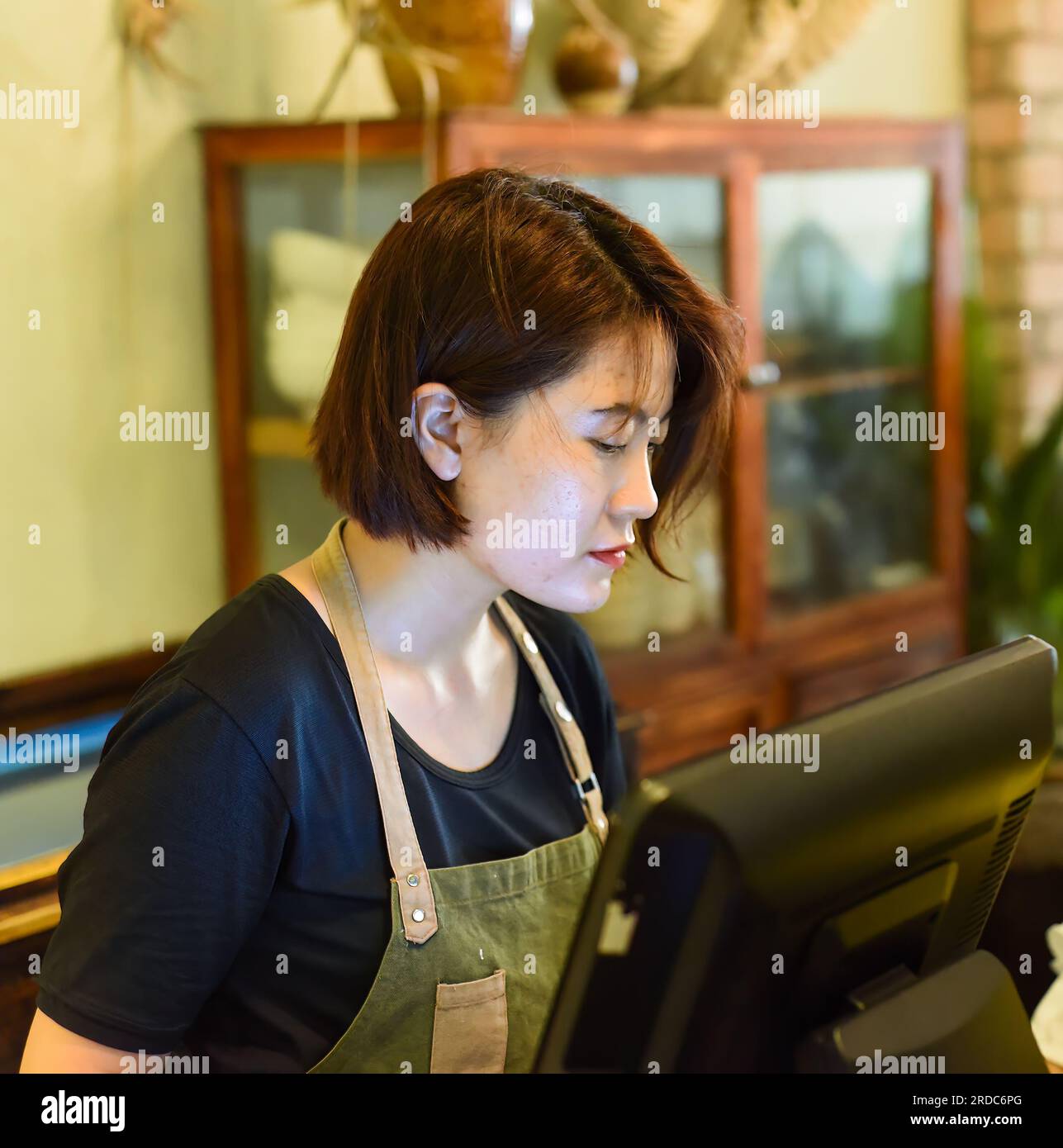 Junge vietnamesische Kellnerin, die mit dem Check-out-Automaten im Café arbeitet Stockfoto