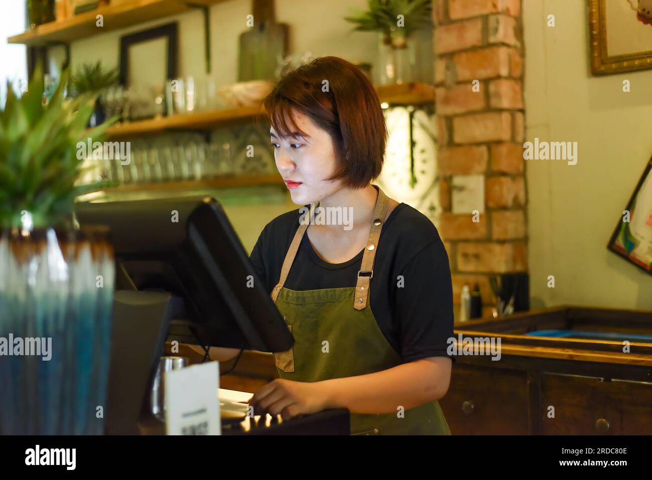 Junge vietnamesische Kellnerin, die mit dem Check-out-Automaten im Café arbeitet Stockfoto