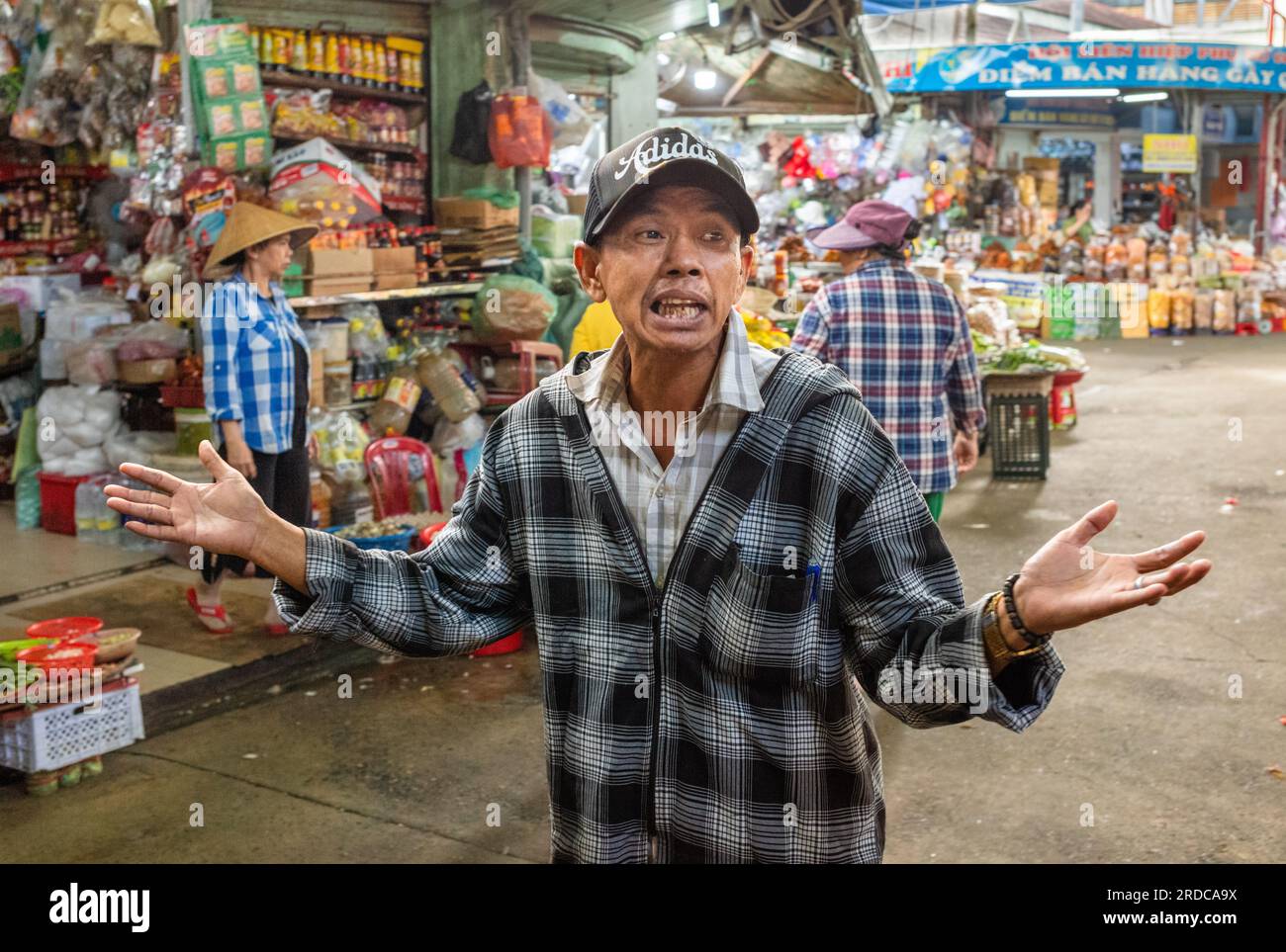 Ein vietnamesischer Mann mit Baseballmütze hält inmitten des Con Market in Danang, Vietnam, an, um zu singen. Stockfoto