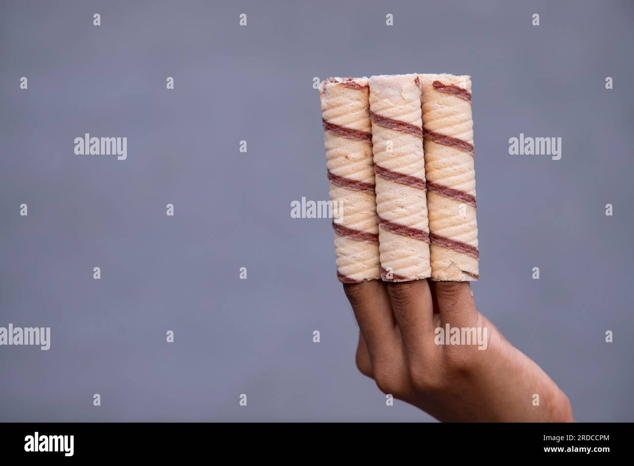 Handgehaltene Waferrollen mit Schokolade auf grauem Hintergrund, Nahaufnahme Stockfoto