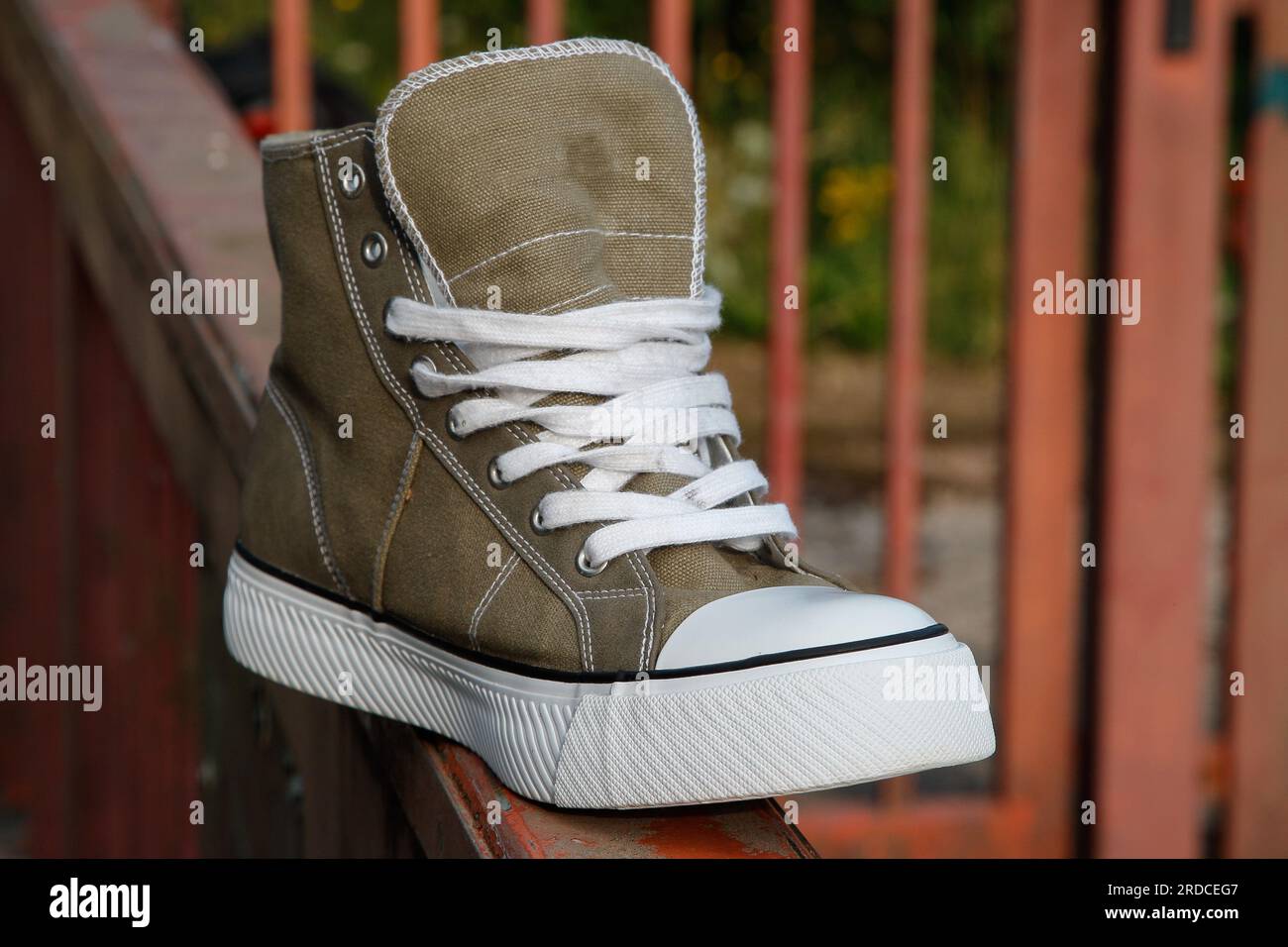 Ein zeitloses Modesymbol auf rotem Stahltor, ein Sneaker aus Segeltuch mit weißer Zehenkappe aus Gummi. Stockfoto