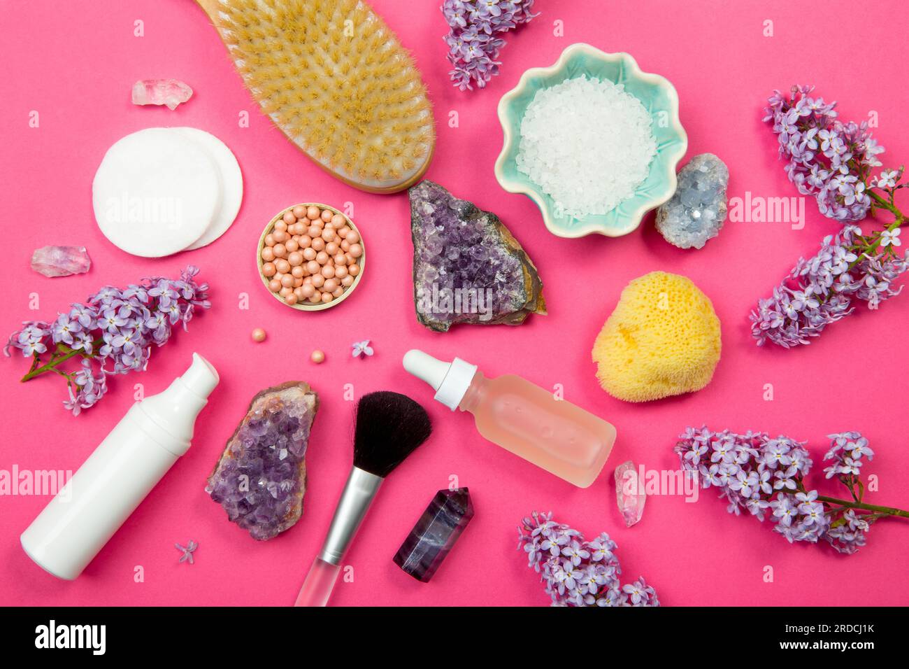 Von oben sehen Sie verschiedene Behälter mit weißen Kosmetik- und Schönheitsprodukten mit Fliederblüten (Syringa) und halbkostbaren Amethyst-Kristallen. Stockfoto