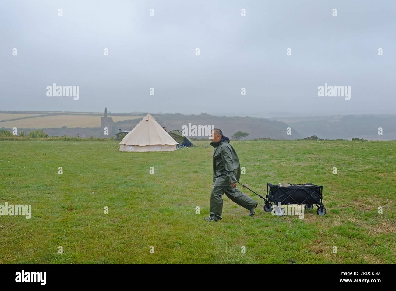 Ein Festivalbesucher, der bei schlechtem Wetter ein leeres Feld verlässt. Stockfoto