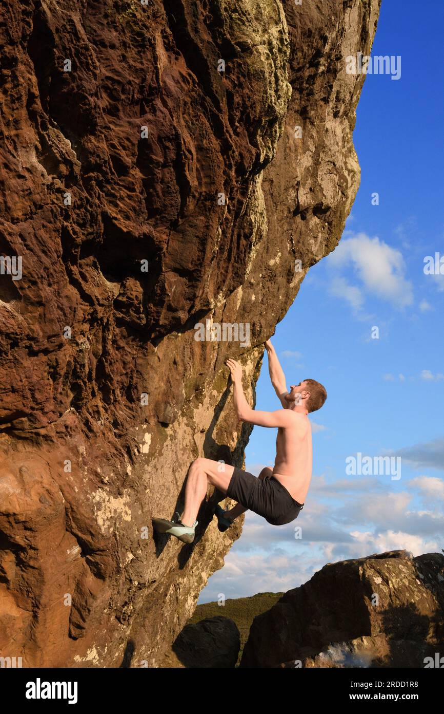 Junger Mann Free klettert auf Agglestone Rock in Dorset Stockfoto