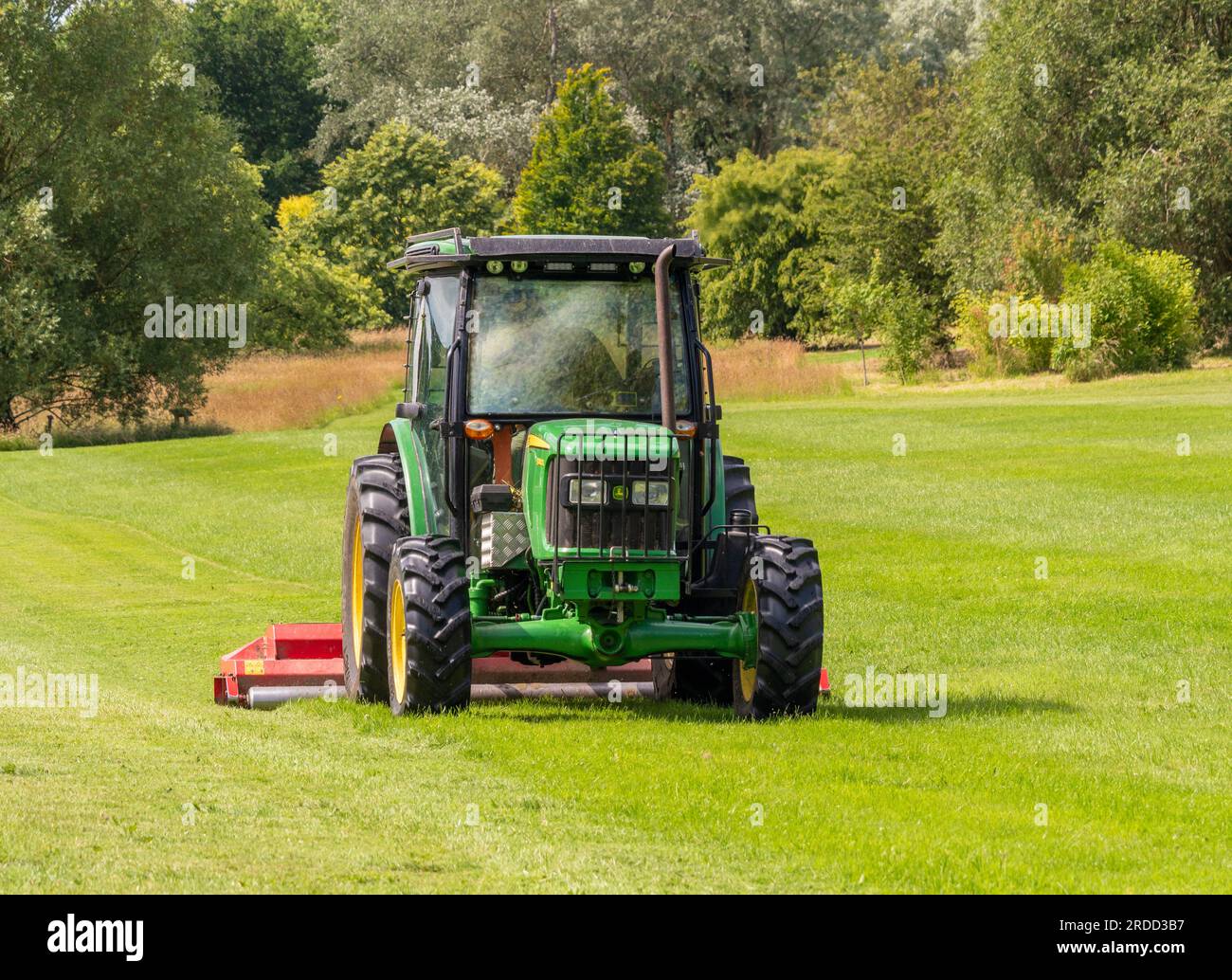 Traktor, der im Sommer an einem sonnigen Tag in einem Parkland das Gras mäht. UK Stockfoto