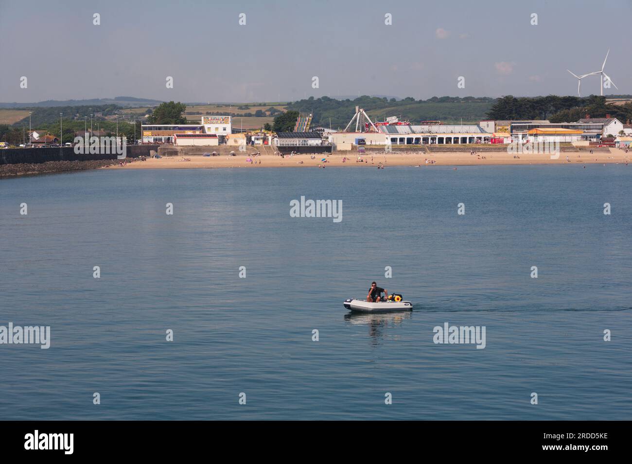 Sandy Bay Porthcwal mit Coney Beach Vergnügungen und Mann im Schlauchboot am ruhigen warmen Juninachmittag Stockfoto