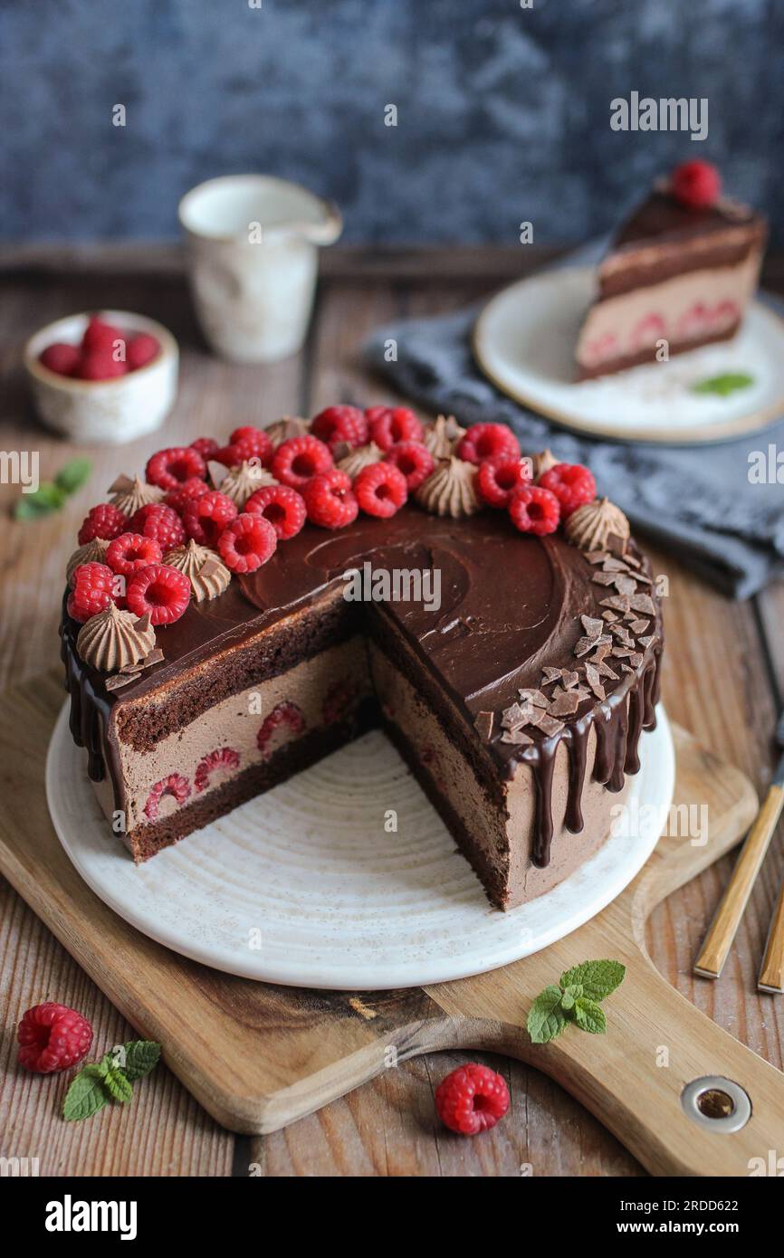 Schokoladen-Himbeerkuchen mit Schokoladen-Ganache und frischen Himbeeren auf der Oberseite. Schneidbrett aus Holz. Blauer Hintergrund. Stockfoto