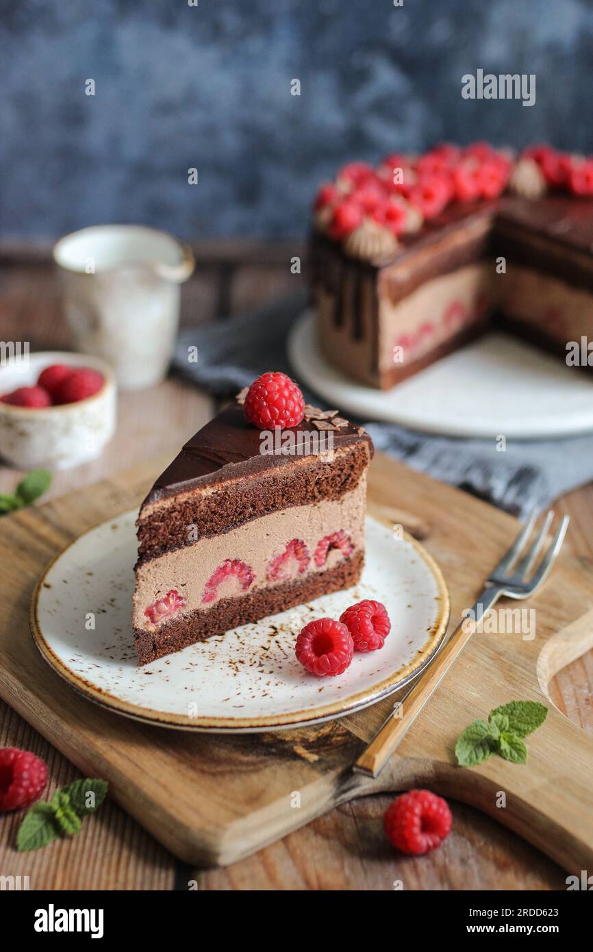 Schokoladen-Himbeerkuchen mit Schokoladen-Ganache und frischen Himbeeren auf der Oberseite. Schneidbrett aus Holz. Blauer Hintergrund. Stockfoto