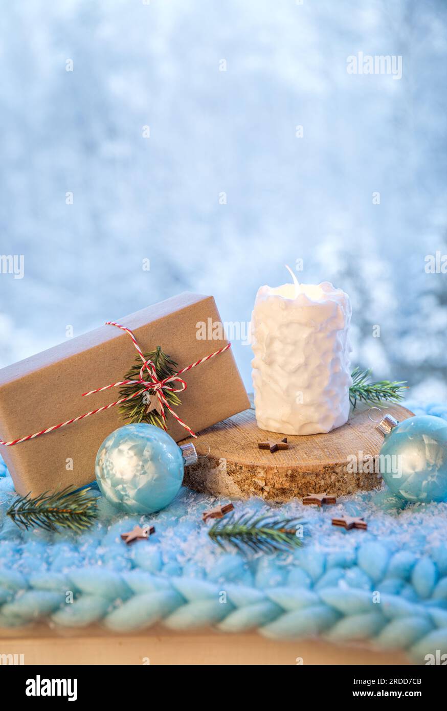 Hintergrundinformationen zu Weihnachtsprodukten. Kerze mit weißem Schneeballmuster brennt, Weihnachtsgeschenk verpackt in braunes Papier mit weiß-roter Schnur. Stockfoto
