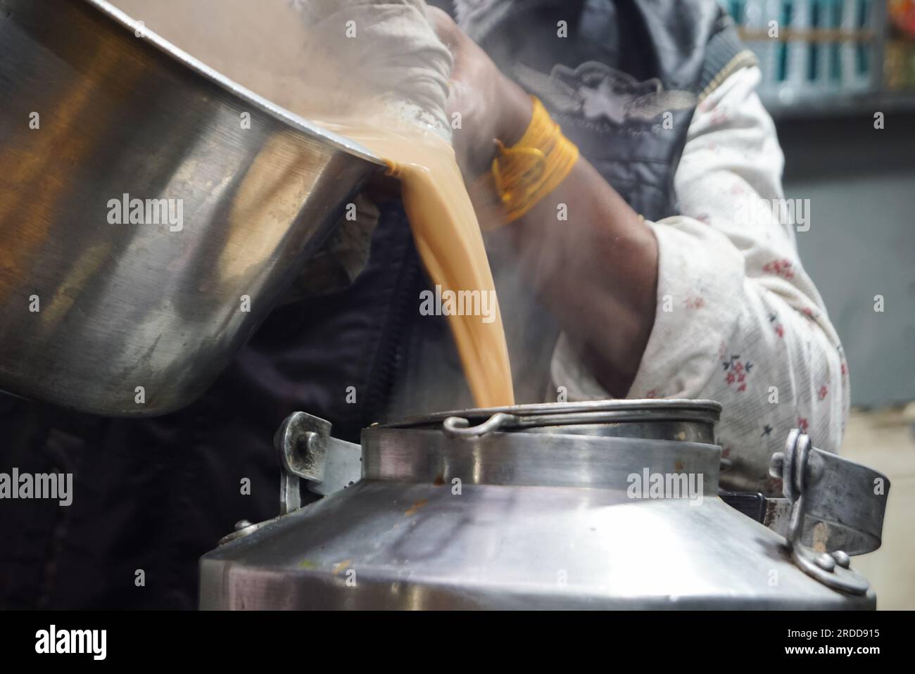 Ich gieße Tee in die Teekanne. Traditionelles indisches Kadak Chai, indisches Garam Chaai, das in Dosen fließt. Bereich Kopieren. Selektiver Fokus. Stockfoto