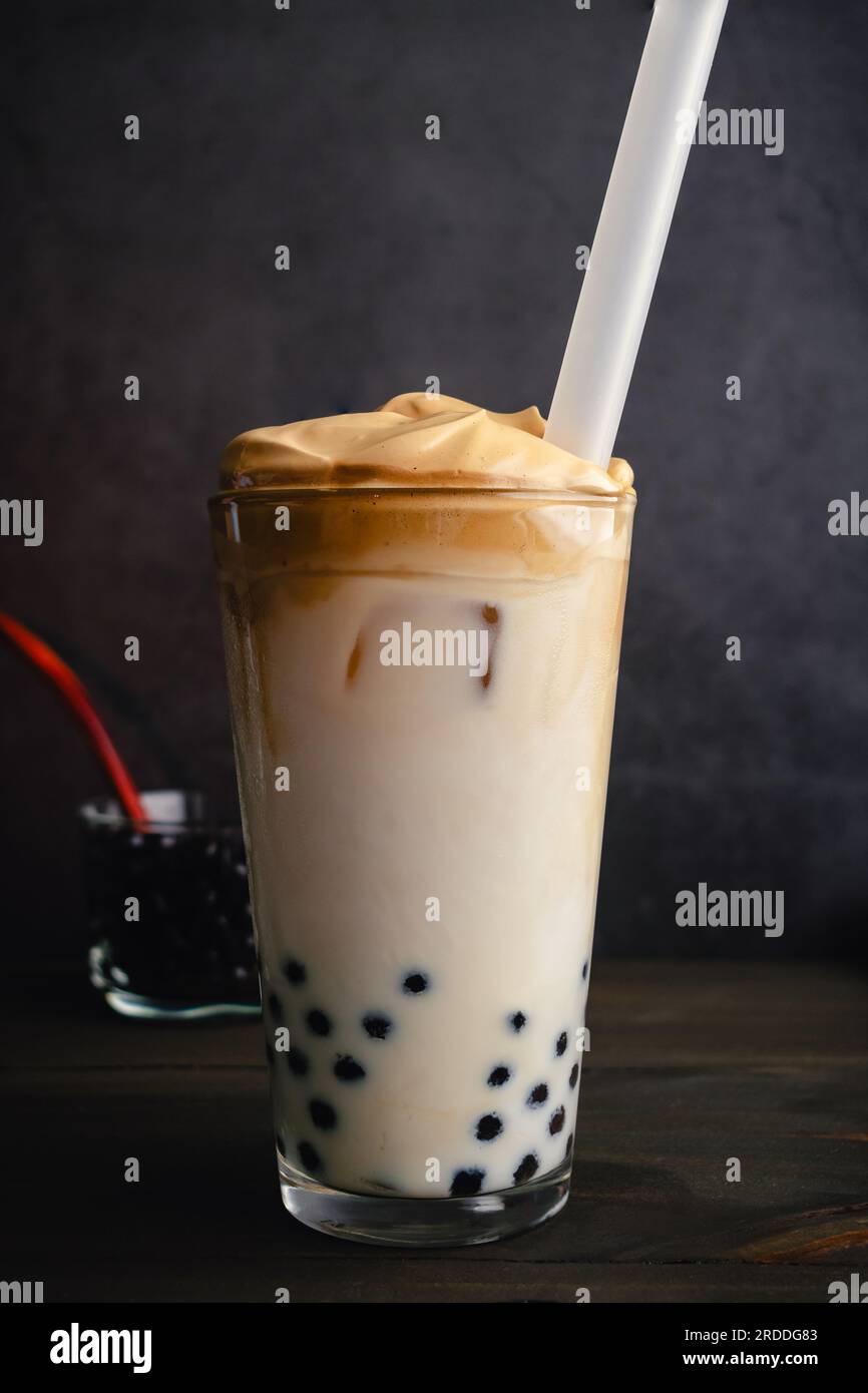 Eisgekühlter Dalgona-Kaffee mit Boba in einem Pint-Glas auf dunklem Hintergrund: Kalter Dalgona-Kaffee mit Milch und Tapiokapperlen mit boba-Strohhalm Stockfoto