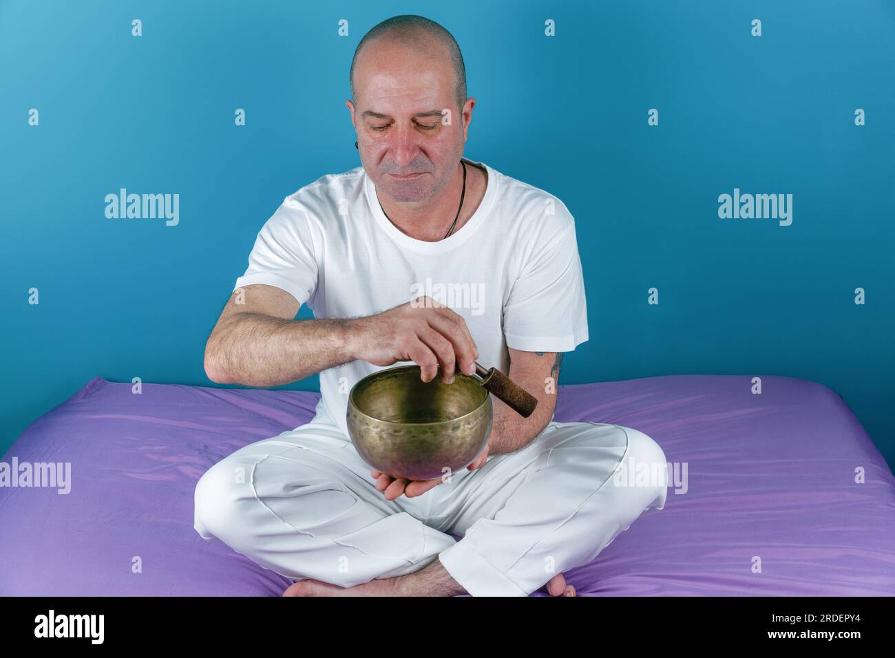 Ein Mann in Weiß, der im Meditationszustand eine tibetische Gesangsschüssel klingt Stockfoto