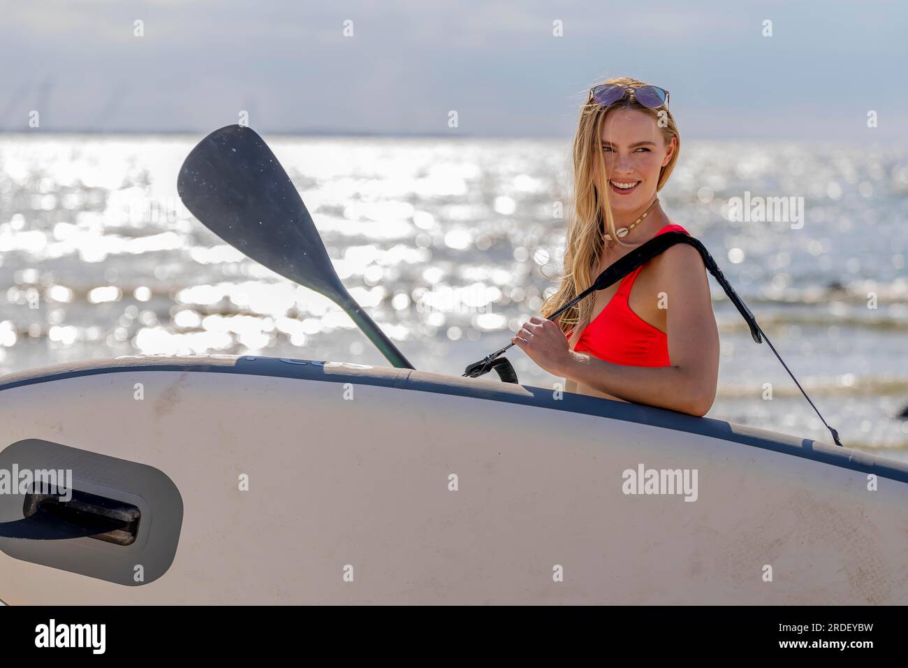 Ein wunderschönes blondes Model genießt einen Sommertag, während es sich mit ihrem Paddle-Board auf das Meer vorbereitet Stockfoto